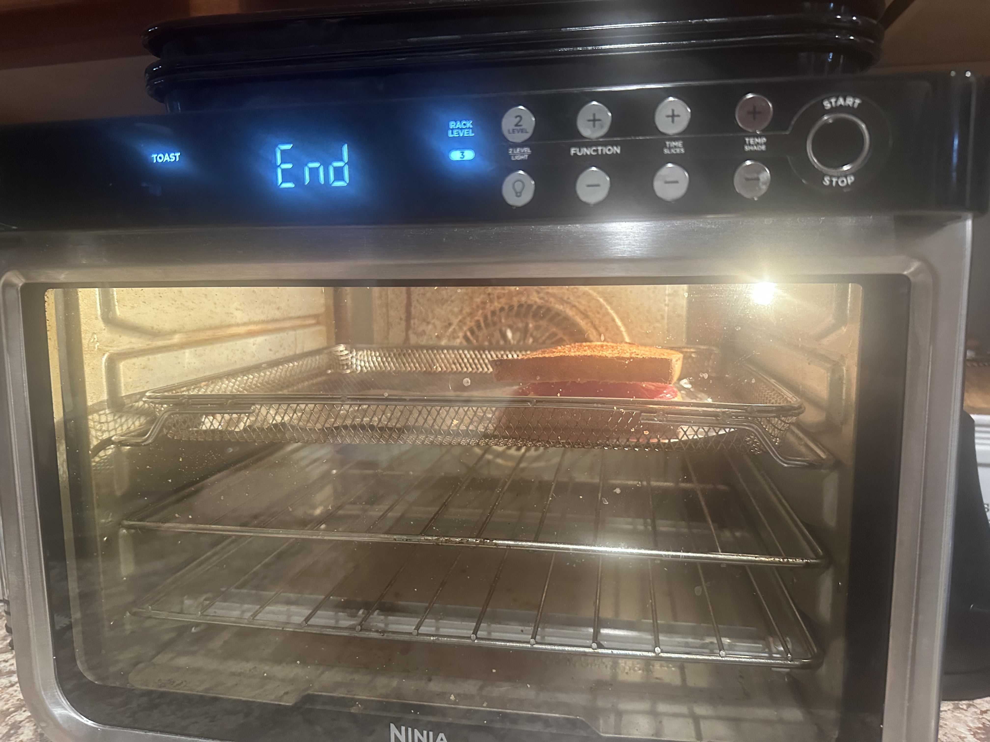 A grilled cheese fully prepeared sitting in a toaster oven, with the toaster oven saying 'End'.