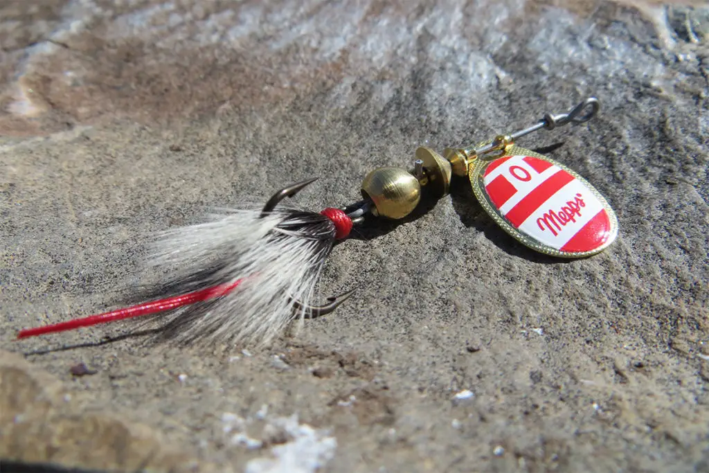 A red and white colored spinner fishing lure laying on rocks.