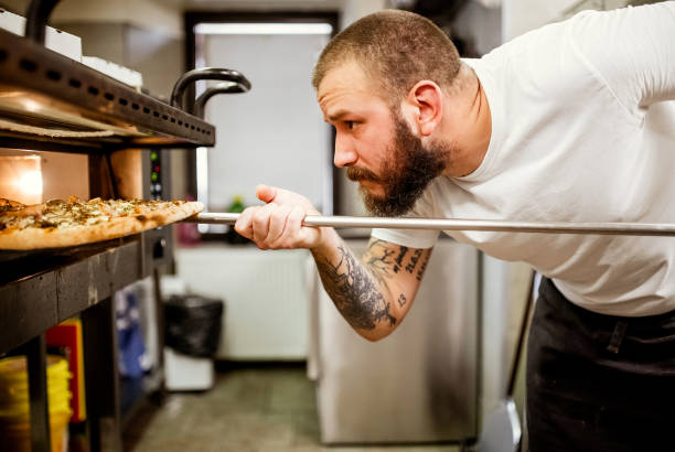 A man setting a pizza that is on a tray into a baking oven.