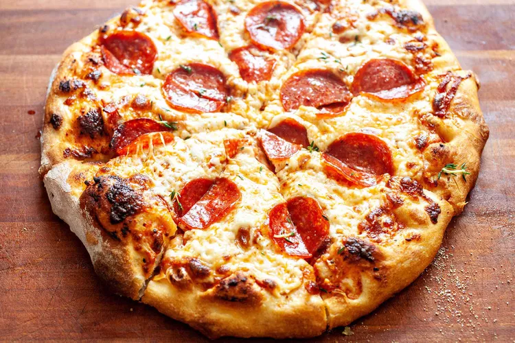 A pizza laid down on a wooden surface, topped with Pepperoni and spices.
